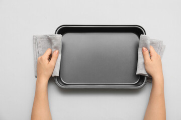 Female hands with towels and baking tray on grey background. Top view