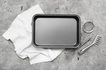 Baking tray, whisk, sieve, tongs and napkin on grey grunge background. Top view
