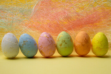 Easter eggs sit in a row against yellow background with colorful fiber filling