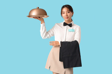 Beautiful Asian waitress with tray and cloche on blue background