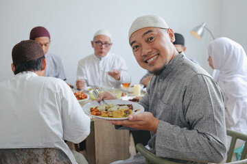 Smiling Young Asian Muslim Man Showing His Food During Eid Mubarak Celebration With Family