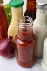 Tasty sauces in glass bottles on white marble table, closeup
