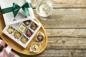 Box with tasty sweets in shape of baubles and wine on wooden background, flat lay. Space for text
