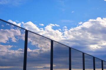 Security fence reflecting clouds and sky in airport perimeter