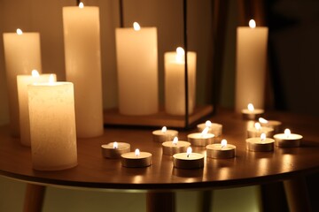 Many burning candles on wooden table, closeup