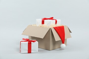 Parcel with gift boxes and Santa hat on light background