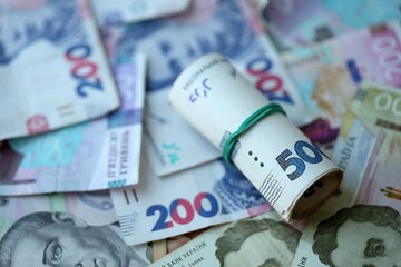 Roll of 500 Ukrainian Hryvnia money bills lies on big pile of ukrainian currency money close up