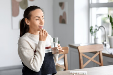 Woman taking medicine in kitchen