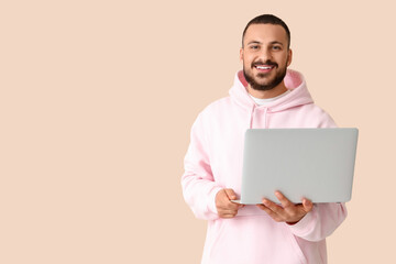 Smiling young man with laptop on beige background