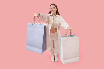Young woman with shopping bags on pink background