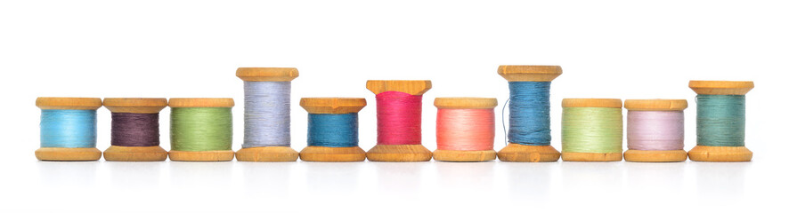 A row of old retro sewing colored thread spools reflections isolated white