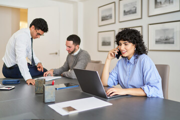 Obraz premium Businesswoman talking on phone and working on laptop in office with colleagues