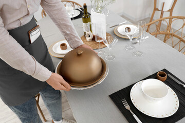 Male waiter putting cloche on table in restaurant, closeup