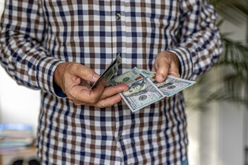 Close-up of a man checking a wad of 100 American dollar banknotes. Cash in hand concept - wages,...