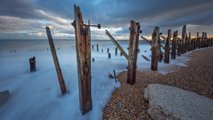 Rotting wooden support posts on the shingle beachwith high tide at sunset , Rye Harbour, Rye, East Sussex, England, United Kingdom, Europe