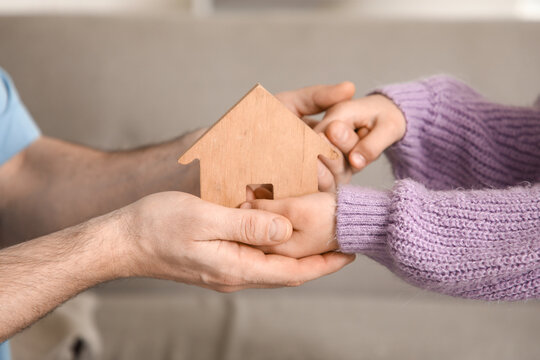 Young man with adopted girl holding wooden house at home, closeup