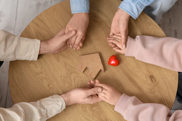 Couple with adopted girl holding hands and house figure on table, top view