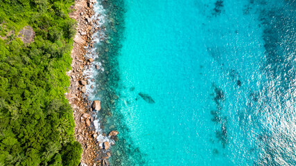 Aerial view of a rocky coast merging with clear turquoise waters and dense greenery. Praslin,...