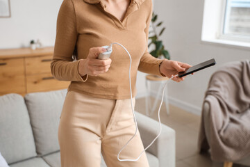 Young woman with modern power bank charging mobile phone at home, closeup