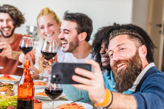 Happy friends taking selfie and drinking red wine at restaurant table