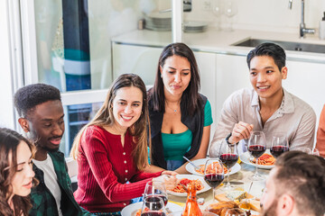 Happy multi-ethnic friends eating pasta and drinking red wine during lunch at home
