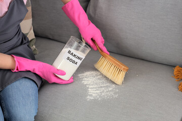 Young woman with baking soda cleaning sofa in room, closeup