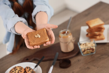 Teenage girl holding toast with nut butter at table in kitchen, closeup