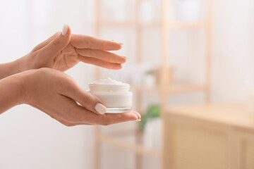 Young woman holding jar of cream in bathroom, closeup