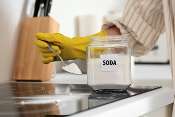 Young woman with baking soda cleaning electric stove in kitchen, closeup