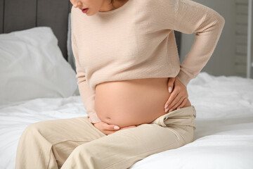 Young pregnant woman suffering from back pain on bed in bedroom, closeup