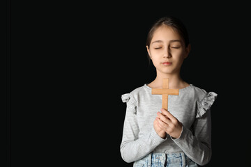 Little girl holding cross on black background