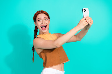 Cheerful young woman with braided hair taking a selfie against a vibrant teal background showcasing her stylish and trendy personality