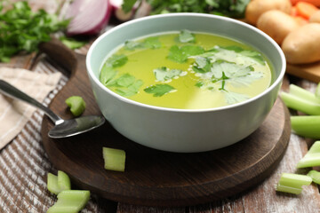Tasty chicken bouillon in bowl and ingredients on wooden table, closeup