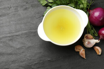 Tasty chicken bouillon in bowl and ingredients on black table, flat lay. Space for text