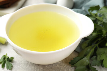 Tasty chicken bouillon in bowl and parsley on grey table, closeup
