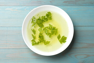 Tasty chicken bouillon with parsley in bowl on light blue wooden table, top view