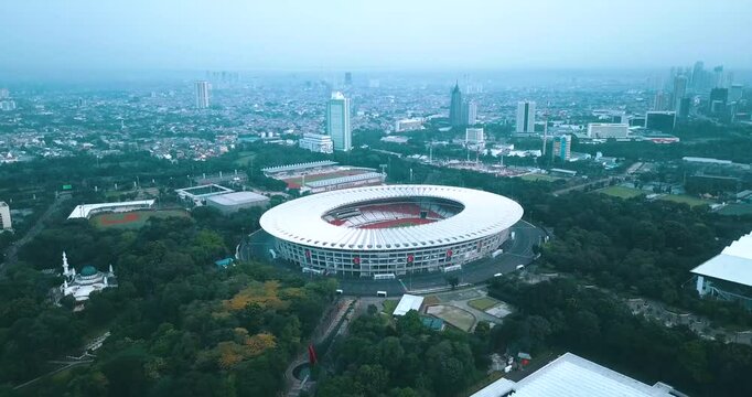 Drone view of Gelora Bung Karno Stadium, Jakarta, Indonesia. This iconic sports complex is surrounded by lush greenery and the city's skyline, showcasing the dynamic blend of nature and urban developm