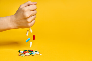 Female hand throws various pills over yellow background