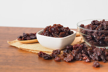Raisins in bowl on wooden table background. Raisins in wooden spoon. Raisins spilling out of jar. Dry raisins.