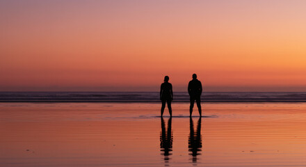 Silhouette of romantic couple standing together on peaceful beach during vivid colorful sunset twilight