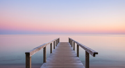 Obraz premium Wooden pier extending into tranquil ocean under pastel sunset sky relaxing calm scenery peaceful view