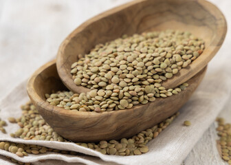 Wooden bowls full of dried raw green lentils on white table closeup. Traditional mediterranean legume