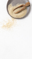 Raw uncooked fonio seeds on grey plate with a wooden scoop on white table topview. African cereal
