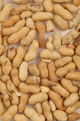 A close-up, top-down view of a scattered pile of raw peanuts in their shells, displaying a variety of textures and natural colors