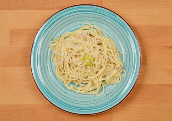 A top-down shot of spaghetti with ham and cream sauce served on a light blue plate, placed on a...