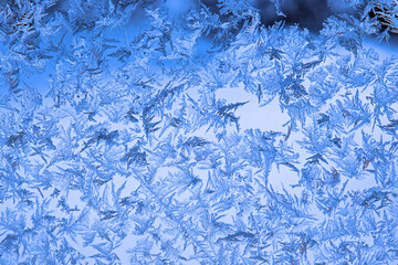 Intricate blue frost pattern on window glass creating an abstract winter background with copy space