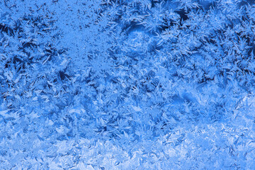 Intricate blue frost pattern on window glass creating an abstract winter background with copy space