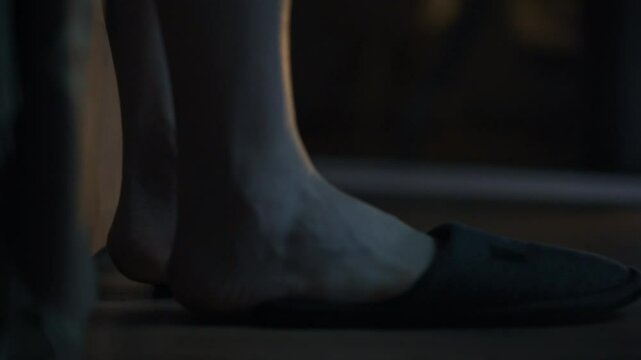A guy gets out of bed in the middle of the night, puts on his slippers and goes to the kitchen. Close-up of his feet as he puts on his slippers and heads to the bathroom. Everyday life of young people
