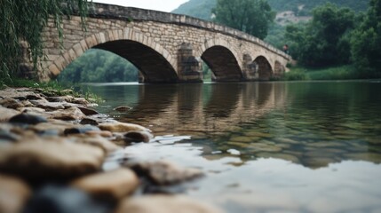 Fototapeta premium An ancient stone bridge reflects gracefully in the still river, embraced by lush nature and a serene atmosphere.
