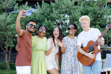 A group of multiracial friends having fun and drinking wine, taking selfies in the summer picnic